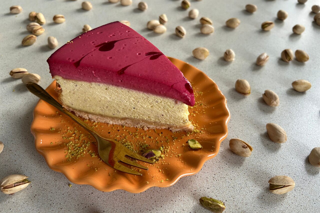 Sernik na herbatnikowym spodzie z pistacjową masą serową i musem malinowym, ozdobiony wzorem z malinowych serduszek